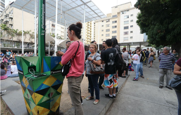 Personas hacen fila para recargar la batería de sus teléfonos móviles en un punto público durante el apagón eléctrico en Caracas. Foto: EFE.