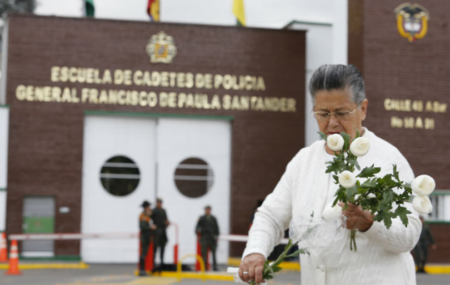 Una mujer porta flores ante la academia atacada con explosivos. Foto: EFE.