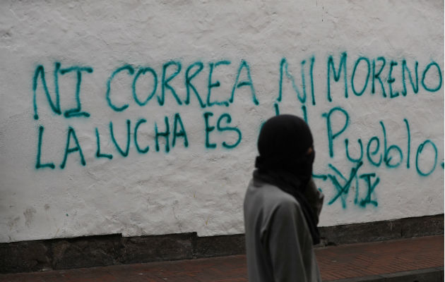 Un encapuchado camina ante una pared con una frase contra el Gobierno. Foto: EFE.