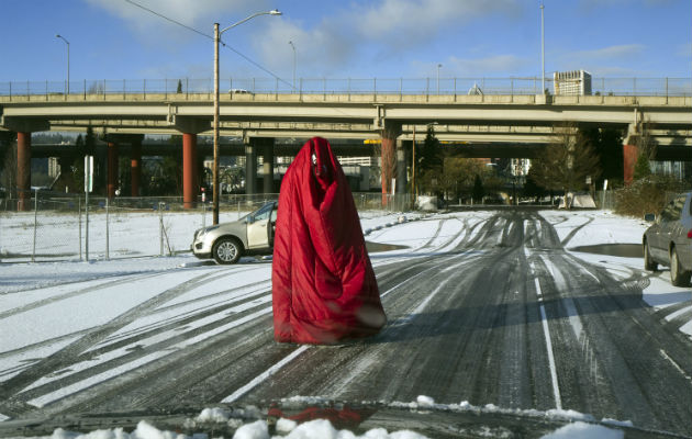 Un hombre camina por la calle cubierto con una bolsa de dormir ante el intenso frío en Portland, Oregon. Foto: AP.