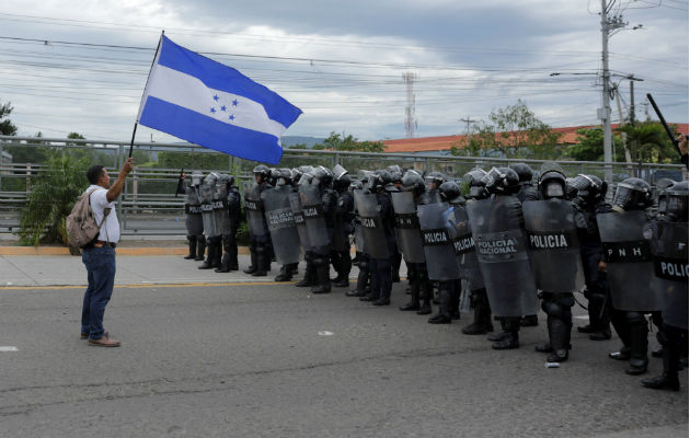  Un manifestante  ondea una bandera hondureña frente a efectivos de la Policía. EFE.