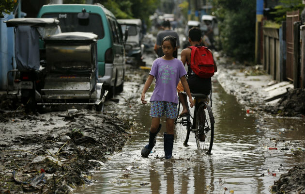 Filipinos transitan por una vía inundada y cubierta de lodo,  debido a las inundaciones. Fotos: EFE 