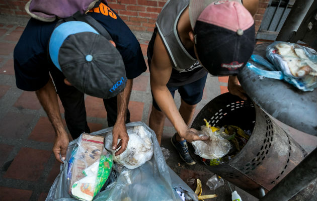 Dos hombres mientras hurgan en una basura en busca de comida en una calle de Caracas. Foto: EFE 