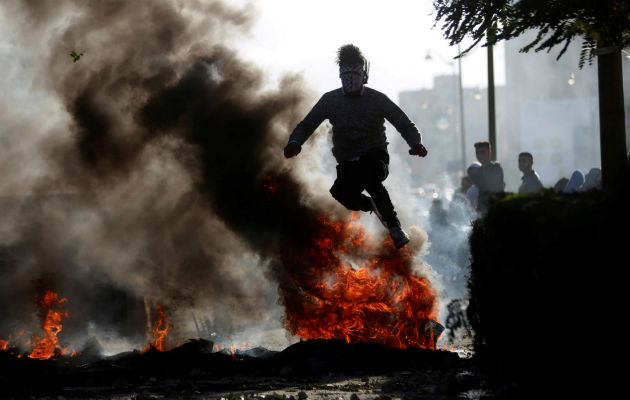 Un manifestante palestino salta sobre un neumático en llamas. Foto: EFE   