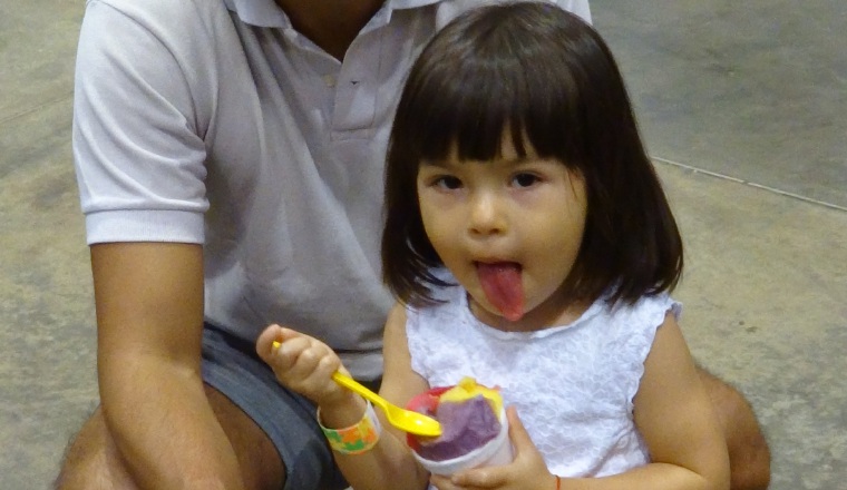 Reya (con su papá) saboreó un raspa'o y muestra su lengua roja. Reya (con su papá) saboreó un raspa'o y muestra su lengua roja.