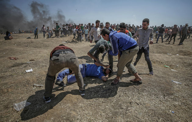 Manifestantes palestinos tratan de ayudar a un herido durante enfrentamientos tras una protesta cerca de la frontera con Israel .FOTO/EFE