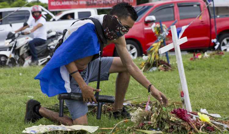 Un joven con una bandera de Nicaragua en la espalda y un lanza morteros en su mano rinde un homenaje en un altar. FOTO/EFE