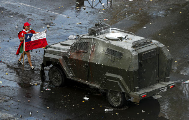 Un manifestante enfrenta con una bandera a un vehículo blindado en Santiago. Foto: AP.
