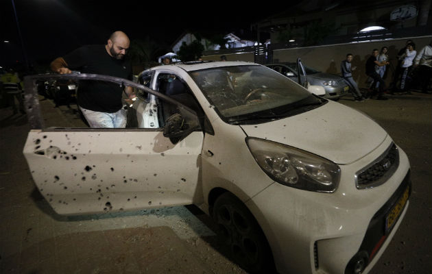 Un israelí observa su vehículo impactado por misiles tirados desde la Franja de Gaza. Foto: AP.