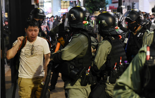 Un hombre afectado por gas pimienta camina ante policías antidisturbios. Foto: EFE.