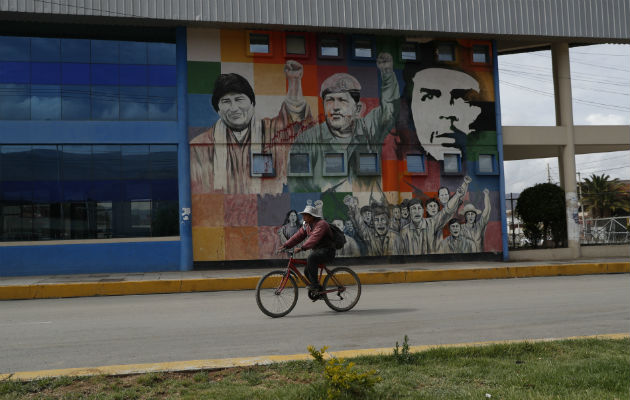 Un ciclista pasa por un mural en una calle boliviana donde aparece el rosto del 