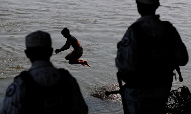 Migrantes hondureños se bañan en el río Suchiate mientras un miembro de la Guardia Nacional de México está de guardia en Ciudad Hidalgo, en la frontera mexicana con Guatemala. FOTO/AP