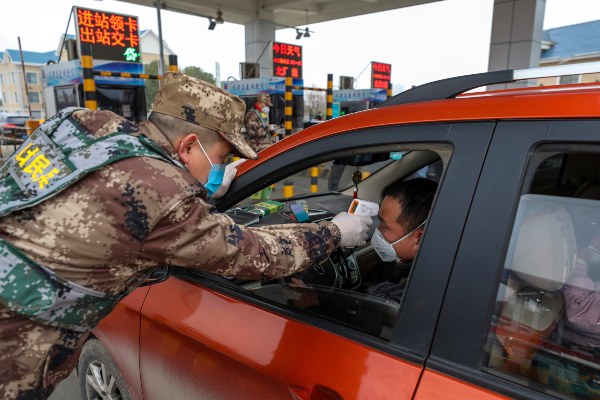 Un miembro de la milicia utiliza un termómetro digital para medir la temperatura del conductor en un punto de control en una puerta de peaje de una autopista en Wuhan. FOTO/AP