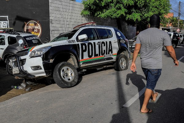 Un hombre encapuchado -supuestamente agente de la policía- camina frente a un vehículo de la institución visiblemente dañado. FOTO/EFE