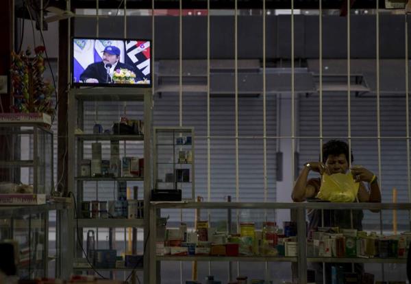 Una mujer realiza compras en una tienda de abarrotes mientras en la pantalla de un televisor aparece el presidente de Nicaragua, Daniel Ortega, durante una transmisión de Cadena Nacional en Managua FOTO/EFE