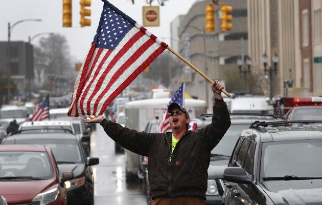   Un manifestante en Michigan entre una fila de autos pasando frente al Capitolio Estatal y tocando el claxon para protestar por los cierres. Foto / Paul Sancya/Associated Press.