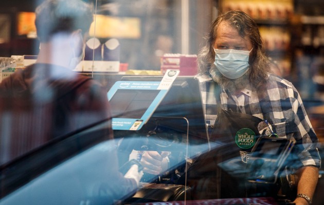 Un empleado de Whole Foods Market con cubrebocas durante la pandemia de coronavirus, frente a una caja registradora, en Washington. (Ting Shen/The New York Times)