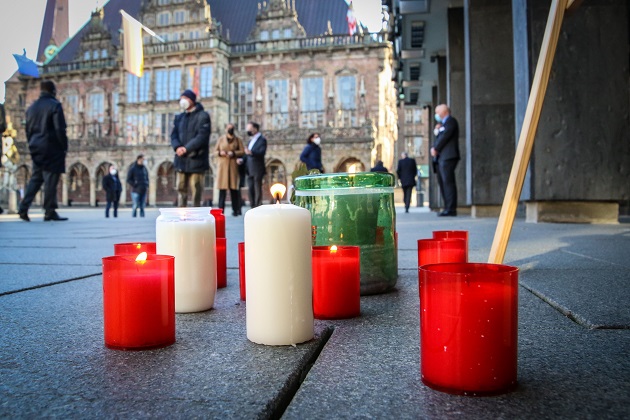 Velas encendidas reposan sobre el pavimento durante una ceremonia para conmemorar las muertes de coronavirus frente al parlamento estatal de Bremen. Foto: EFE