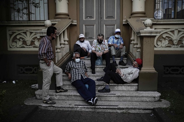  Varios hombres, algunos sin el uso correcto del tapabocas, conversan en las escalinatas de un edificio en una calle de San José, Costa Rica. Foto: EFE