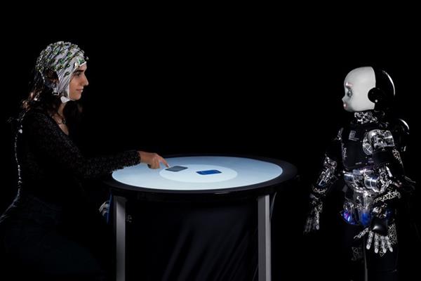 Una persona y un robot humanoide participan en un juego competitivo, mientras se mide su actividad cerebral con un electroencefalograma. Foto: EFE