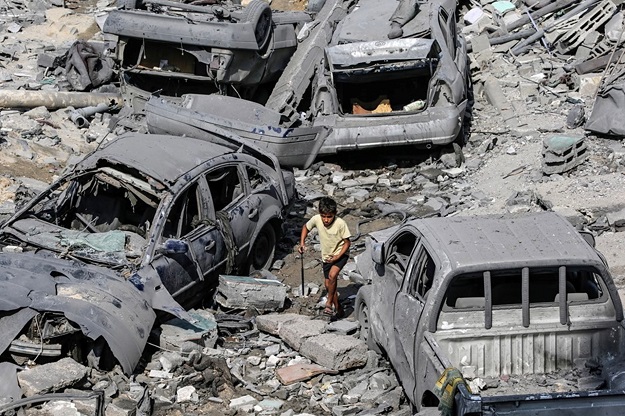 Un niño palestino pasa junto a coches dañados en los ataques aéreos israelíes en la ciudad de Gaza. Foto: EFE/Mohammed Saber