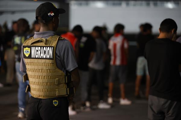 Un agente de migración de Panamá vigila a migrantes antes de ser deportados a Colombia. EFE/ Bienvenido Velasco