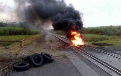 Moradores de Gold Hill queman cauchos y portan pancartas en protesta por la falta de señalización en el cruce ferrovial. Foto: Delfia Cortés.<br>