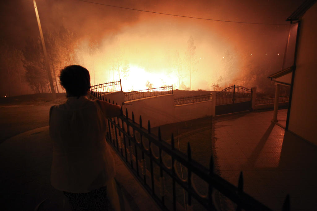 Una mujer mira el fuego se aproxima a una casa en Ribeira do Farrio, cerca de Ourem, Portugal. Foto/AP<br>