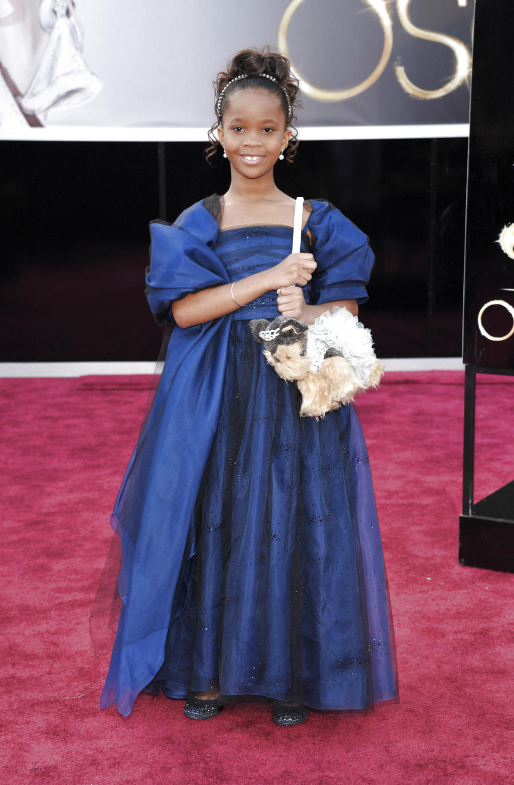 Quvenzhane Wallis con una cinta plateada en el cabello y su carterita de peluche, lució un Armani Junior azul marino con negro y acentos plateados salpicados en la falda,. AP<br>