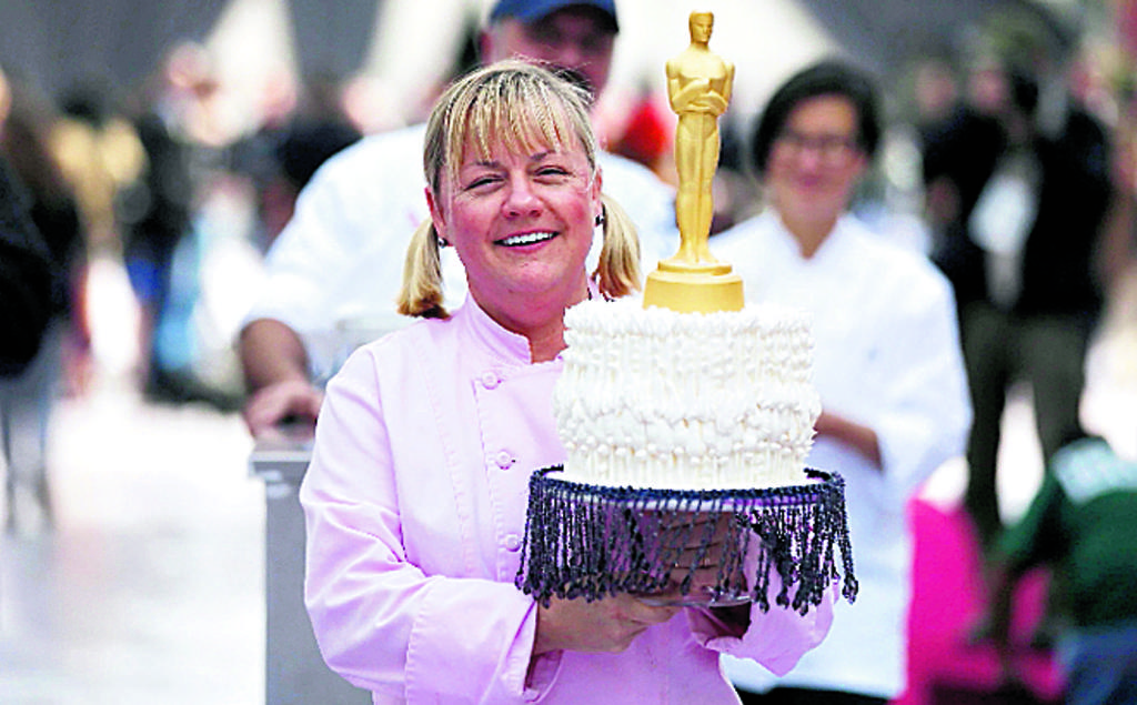 Sherry Yard, quien es una chef ejecutiva de repostería del grupo de restaurantes Wolfgang Puck, lleva un pastel decorado con una estatua de Óscar, mientras camina a través del área de la alfombra roja del teatro.
