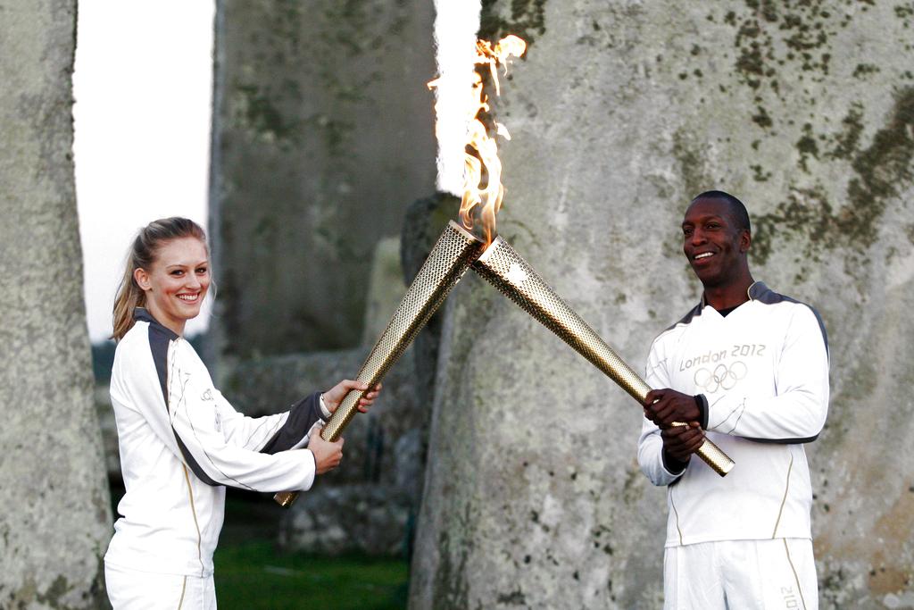 El exatleta olímpico estadounidense Michael Johnson (dcha) le pasa el relevo de la antorcha a Emilia Clifford en Stonehenge (Reino Unido). Foto: EFE<br>