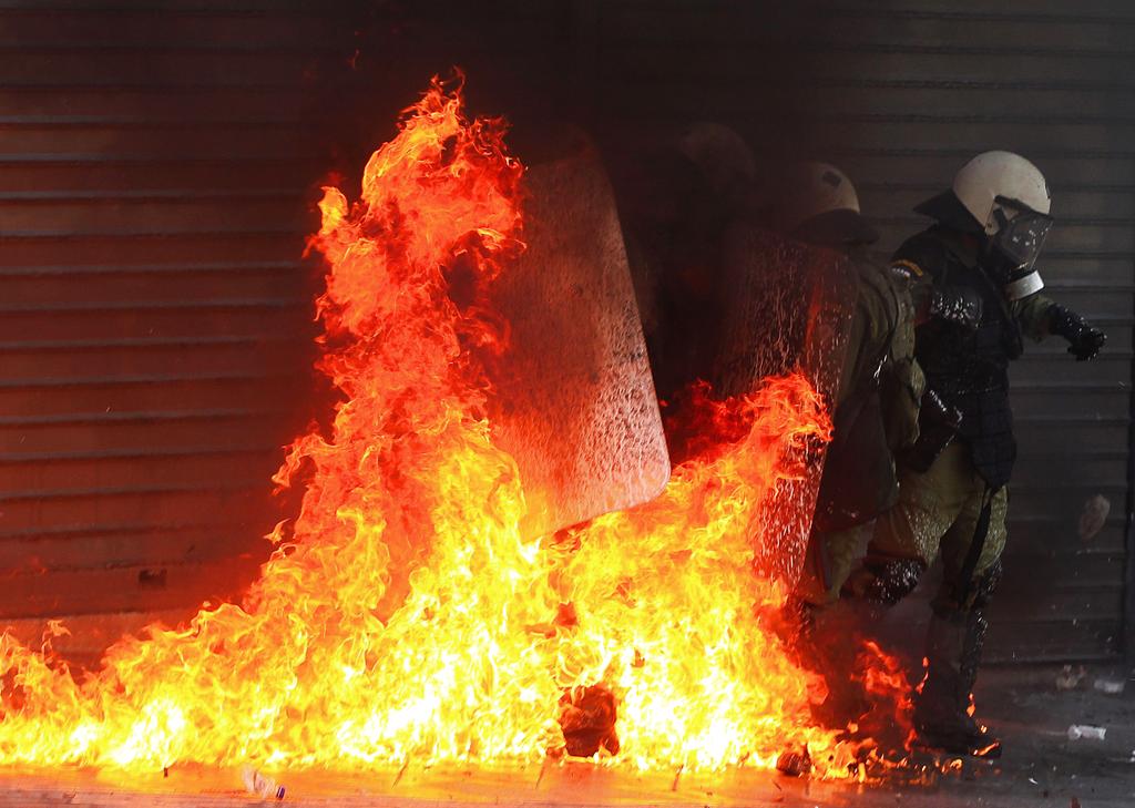 Policías antidisturbios se ven envueltos por las llamas de una bomba incendiaria. Foto/EFE