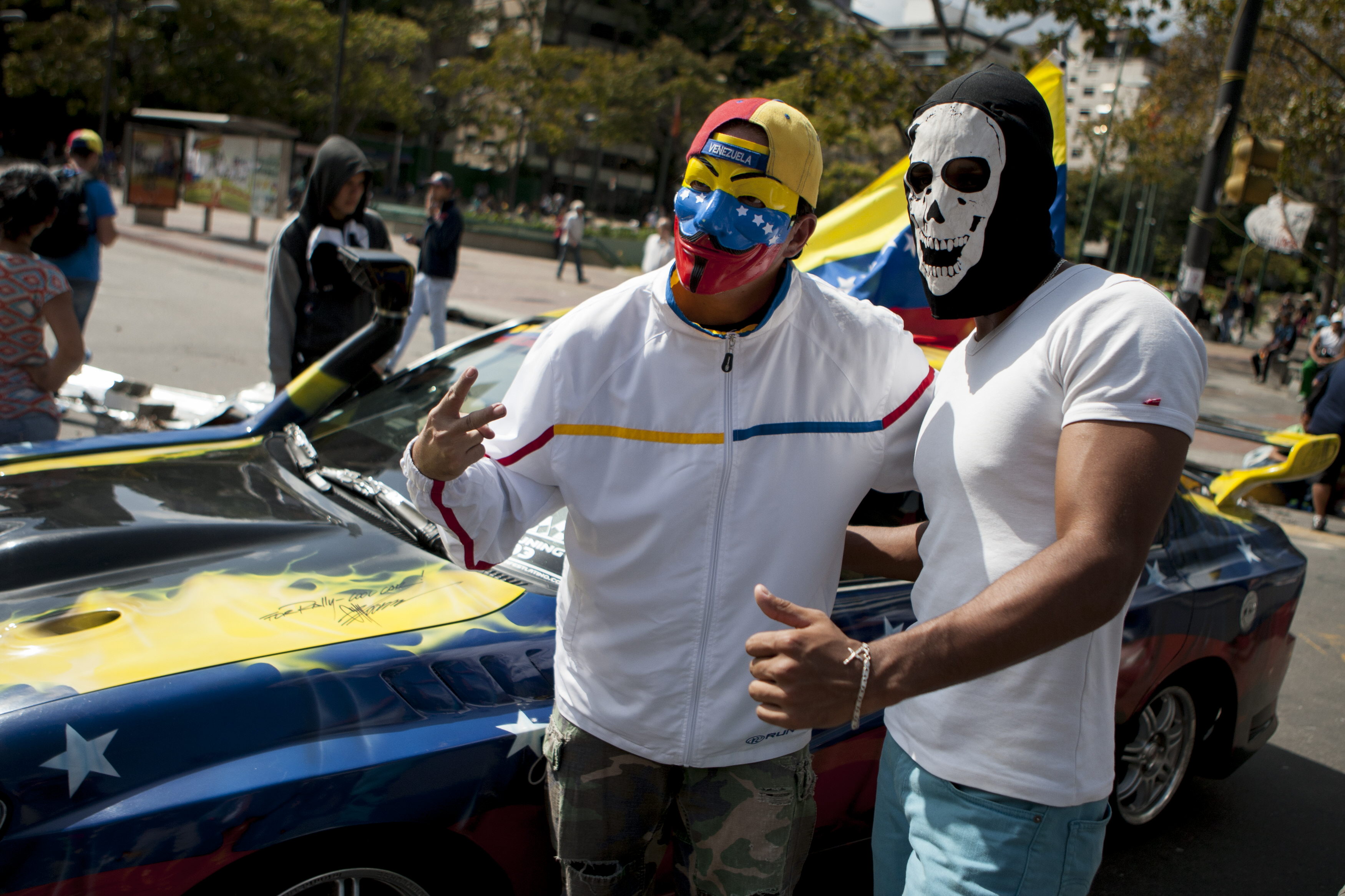 Dos jóvenes opositores enmascarados posan junto a su auto en una barricada en la Plaza Altamira en el este de Caracas. Foto/EFE