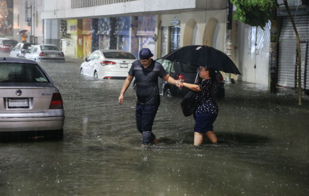  Dos personas cruzan una calle inundada en el puerto de Acapulco por el huracán Rosa. 