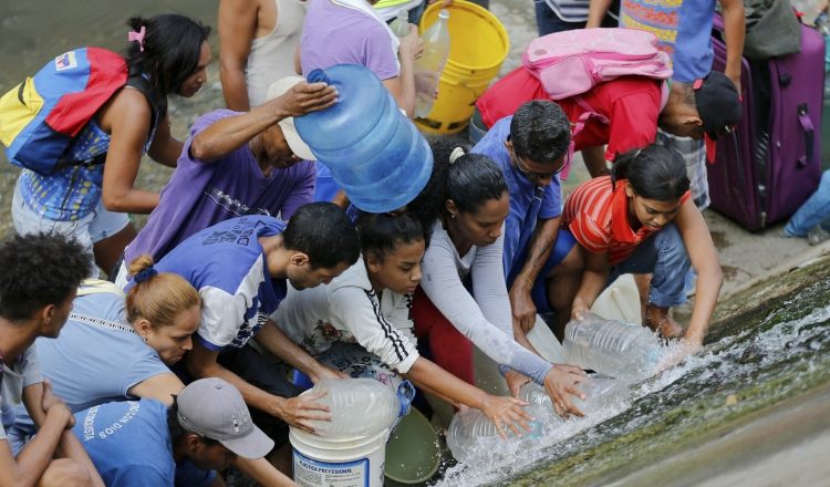 Venezolanos recogen agua de una tubería rota cerca al río Guaire, en Caracas. AP