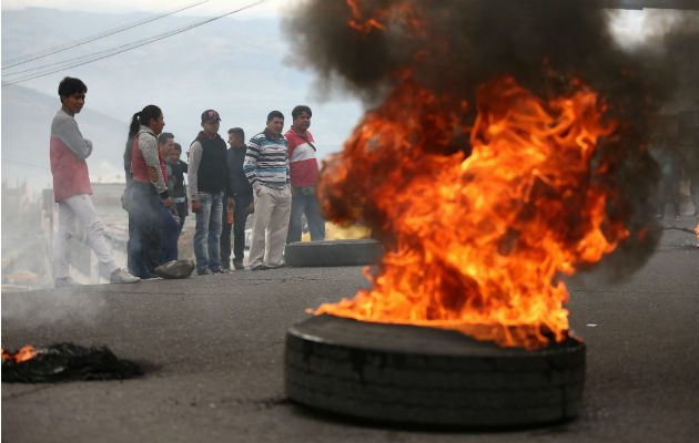 Un encapuchado camina ante una pared con una frase contra el Gobierno. Foto: EFE.