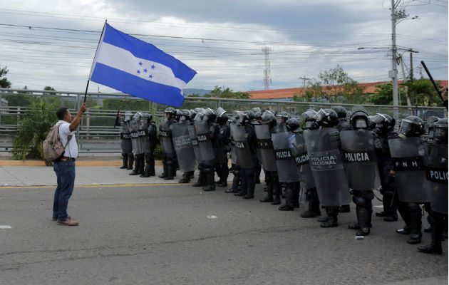 Un manifestante  ondea una bandera hondureña frente a efectivos de la Policía. EFE.