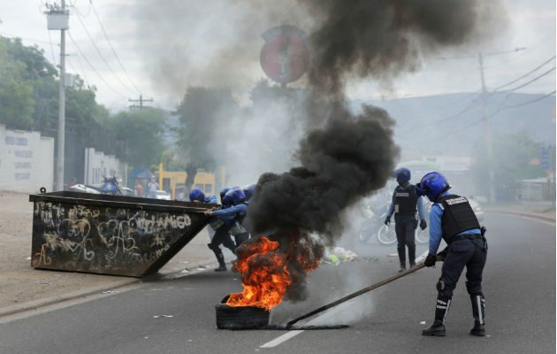 Un policía quita neumáticos en llamas tras enfrentamientos con manifestantes en Tegucigalpa. Foto: EFE.
