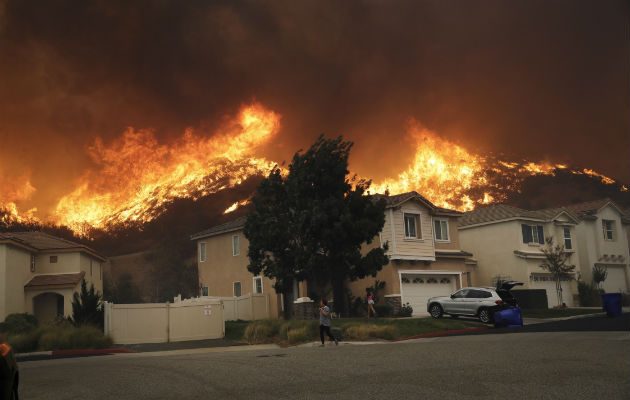 Un joven camina cubriéndose la nariz del humo causado por el fuego en Santa Clarita. Foto: AP.