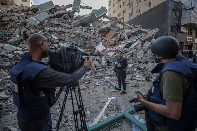 El equipo de televisión palestino trabaja junto a los escombros de su oficina destruida, la torre Al-Jalaa, que alberga apartamentos y varios medios de comunicación en la ciudad de Gaza. Foto: EFE