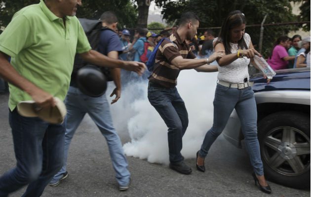Opositores se alejan del gas lacrimógeno lanzado cerca a la tarima de Guaidó. Foto: AP.