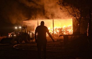 Bomberos y voluntarios combaten un almacén en llamas durante un incendio forestal en la aldea de Feneos, municipio de Corinto, Grecia. Foto: EFE