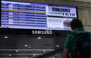 Fotografía de una persona caminando junto a una pantalla con la programación de vuelos, en el Aeropuerto Internacional Simón Bolívar, en Maiquetía (Venezuela). Foto: EFE/ Ronald Peña R.