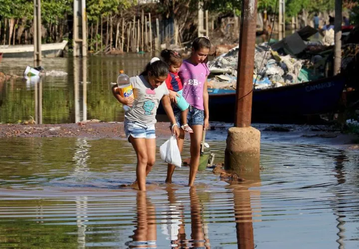 Unos niños caminan rodeados de agua por una de las calles del barrio Bañado Norte, de Asunción. Foto: EFE 