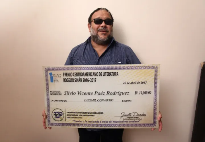 El escritor Héctor Collado, quien leyó el fallo, muestra el cheque a que se hizo acreedor el ganador. /Foto Aurelio Herrera Suira.