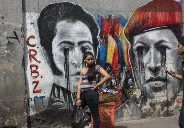 Dos jóvenes en Caracas, frente un graffiti de Simón Bolívar y Hugo Chávez llorando por su país. /Foto AP