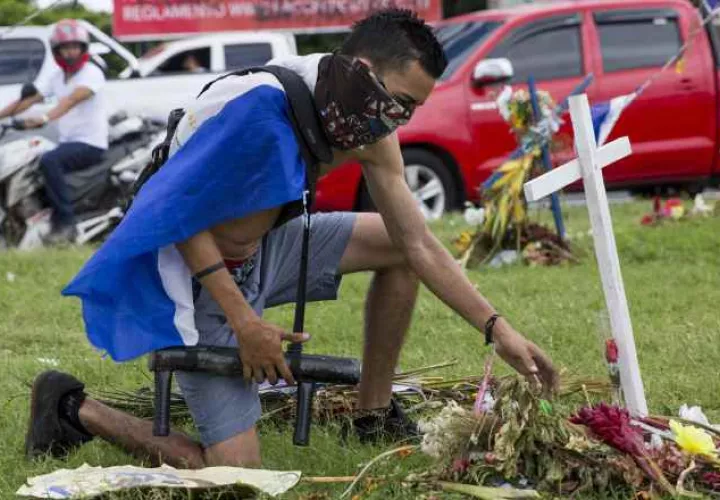 Un joven con una bandera de Nicaragua en la espalda y un lanza morteros en su mano rinde un homenaje en un altar. FOTO/EFE