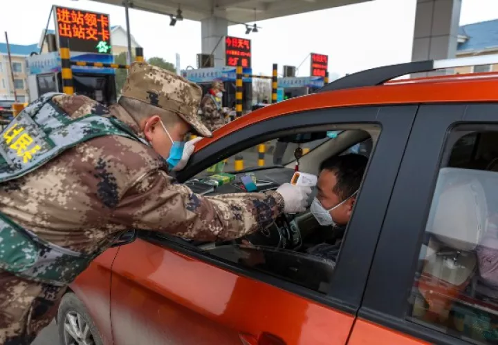 Un miembro de la milicia utiliza un termómetro digital para medir la temperatura del conductor en un punto de control en una puerta de peaje de una autopista en Wuhan. FOTO/AP