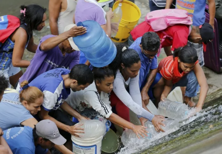 Venezolanos recogen agua de una tubería rota cerca al río Guaire, en Caracas. AP