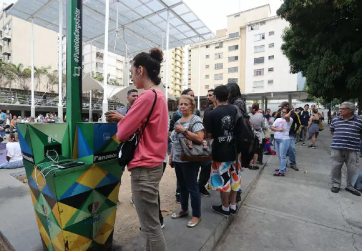 Personas hacen fila para recargar la batería de sus teléfonos móviles en un punto público durante el apagón eléctrico en Caracas. Foto: EFE.